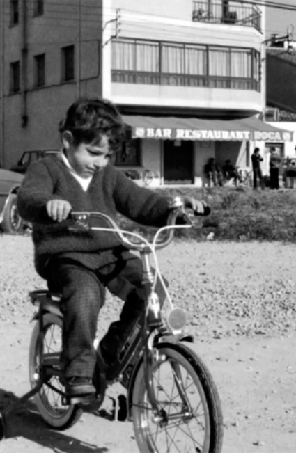 <p><strong>Jordi</strong><span>, en bicicleta por los descampados delante de </span><strong>Can Roca</strong><span>, cuando el barrio de Germans Sàbat, en Taialà, era un barrio naciente, un barrio en construcción. </span><strong>Can Roca</strong><span> estaba situado en un extrarradio de la ciudad que fue engulliendo como pudo la llegada de inmigrantes del sur de España de finales de los años 50 y los 60. El año 2010,</span><strong><span> </span>Josep Roca </strong><span>hizo el pregón de la fiesta mayor de Germans Sàbat.</span></p>